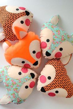 four stuffed animals sitting next to each other on top of a white table with orange and blue pillows