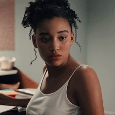 a woman sitting at a desk with a book in front of her and looking into the camera