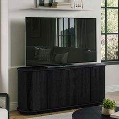 a flat screen tv sitting on top of a wooden cabinet in front of a window