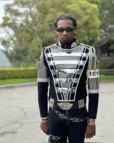 a man with dreadlocks standing in front of a building wearing a black and white suit