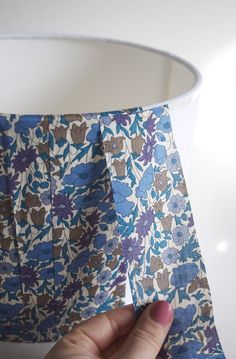 a person holding up a lamp shade with blue and brown flowers on the fabric in front of it