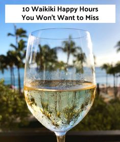 a wine glass filled with white wine sitting on top of a table next to the ocean