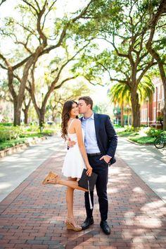 a man and woman kissing in front of trees on a brick walkway with their legs crossed