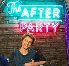 two people sitting at a table in front of a neon sign that says the after party