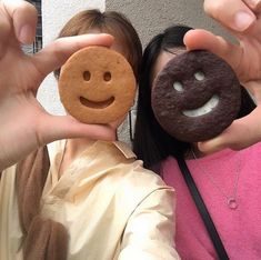 two women are holding up small cookies with faces on them and one has a smiley face