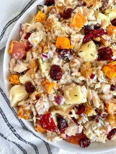 a white bowl filled with fruit salad on top of a striped table cloth next to a fork