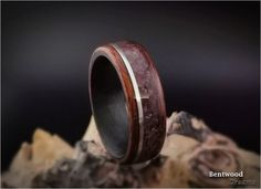 a wooden ring with silver inlays sits on top of a rock and looks like it is made out of wood