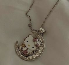 a hello kitty necklace is shown on a white sheet with a chain that has an image of a cat sitting on top of the moon