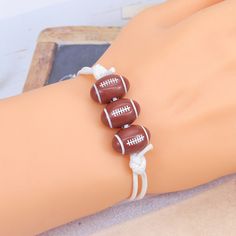 three brown and white football bracelets on a woman's wrist, one is tied to the other