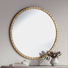 a round mirror sitting on top of a table next to a vase filled with flowers