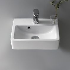 a white sink sitting next to a wall mounted faucet and a vase with flowers