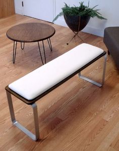 a white bench sitting on top of a hard wood floor next to a chair and table