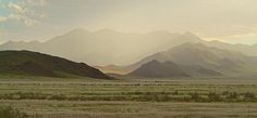 mountains are in the distance with grass and bushes on the ground, as the sun is setting