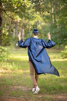 a man in a graduation gown is walking through the woods with his hands raised up