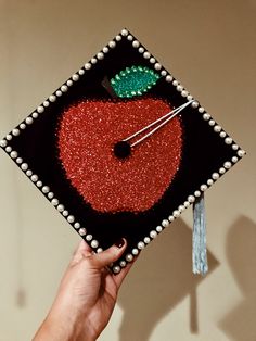 a hand holding up a graduation cap with an apple on the front and tassel