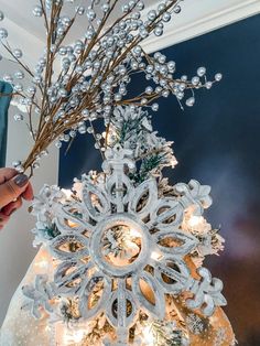 a snowflake tree is decorated with white lights and silver ornaments, while someone holds the branch in their hand