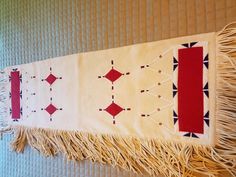 a white and red wall hanging with fringes on it's sides, next to a window