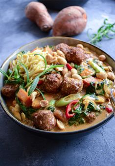 a bowl filled with pasta and meatballs on top of a blue table next to a fork