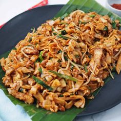 a black plate topped with noodles and meat on top of a leafy green napkin