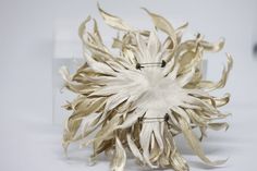 a white and gold sculpture made out of dried leaves on a white surface with an acrylic sign in the background