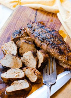 a wooden cutting board topped with meat next to a knife and fork on top of it