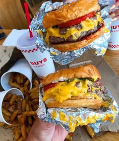 two hamburgers with cheese and ketchup sitting on tin foil next to french fries