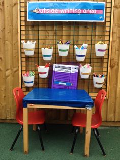 there is a blue table and red chairs in front of a wall with buckets on it