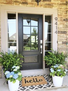 two potted plants are sitting on the front porch next to a welcome mat that says hello