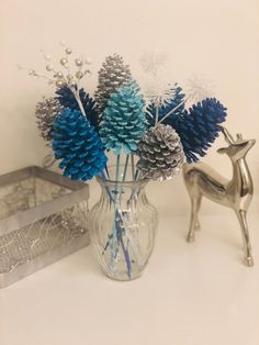 a glass vase filled with blue and silver pine cones