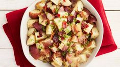 a white bowl filled with potatoes and bacon on top of a red napkin next to a fork