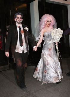 a bride and groom dressed up in zombie costumes are walking down the street holding hands