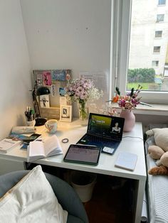 an open laptop computer sitting on top of a white desk next to a flower vase