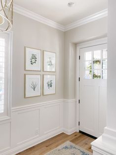 an entryway with white walls and wood flooring, framed pictures on the wall