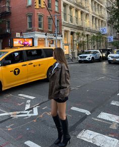 a woman standing in front of a yellow taxi on the side of a road with traffic lights