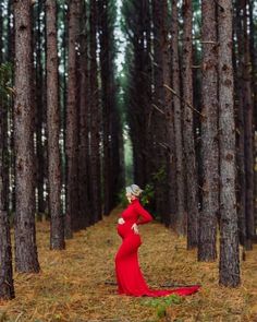 a pregnant woman in a red dress standing in the woods with her hands on her hips