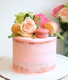 a pink frosted cake with macaroons and flowers on top