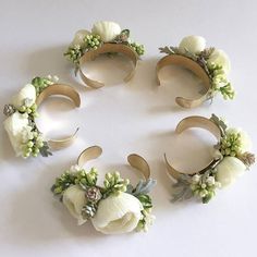 four white flowers and leaves are arranged in the shape of a circle on a table