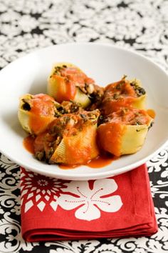 a white bowl filled with stuffed shells covered in sauce on top of a red napkin