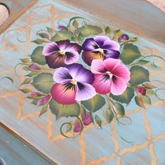 some purple and pink pansies painted on a wooden table with gold trimmings