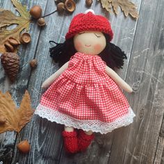 a doll with black hair wearing a red and white checkered dress is laying on a wooden surface