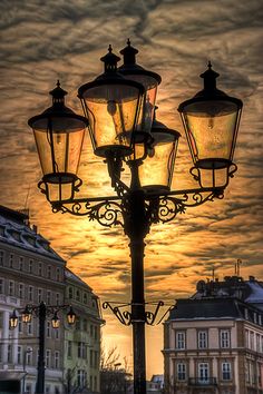 a street lamp with three lights on it in front of a cloudy sky at sunset