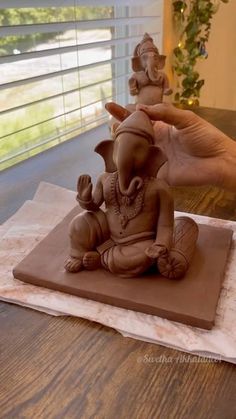 a hand is holding an elephant statue on top of a wooden table next to a window