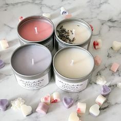 four tins of candles sitting on top of a marble table with hearts around them