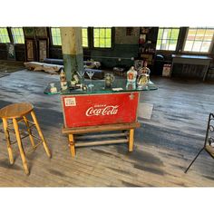 an old coca - cola machine sits in the middle of a room with stools