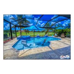 an empty swimming pool with blue umbrellas and chairs under the shade in front of it