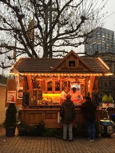 two people standing at a small bar with lights on the roof and trees in the background