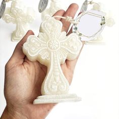 a hand holding a small white cross shaped object in it's left hand with other decorations around it