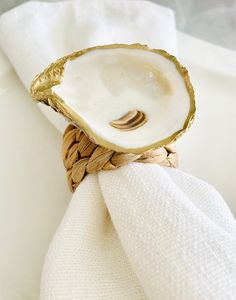 an oyster shell napkin ring on top of a white napkin with gold trimmings