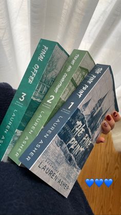 the person is holding five books in their hand, all stacked on top of each other