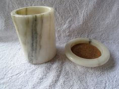 a marble cup next to a white vase filled with sand on a white toweled surface